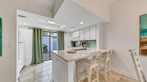 A modern kitchen with white cabinets, a central island with bar stools, a microwave, and a sink. - Pet-friendly Fenced Yard, Linkside Village 476! (Destin)
