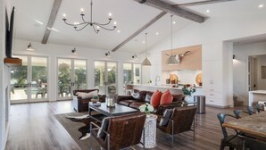 A spacious living area with a large dining table, leather sofas, and a chandelier.