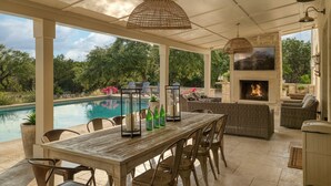 A covered outdoor area with a pool, seating, and a fireplace.