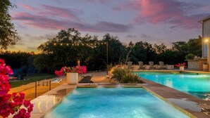 A swimming pool with a stone deck, surrounded by potted plants and outdoor furniture.
