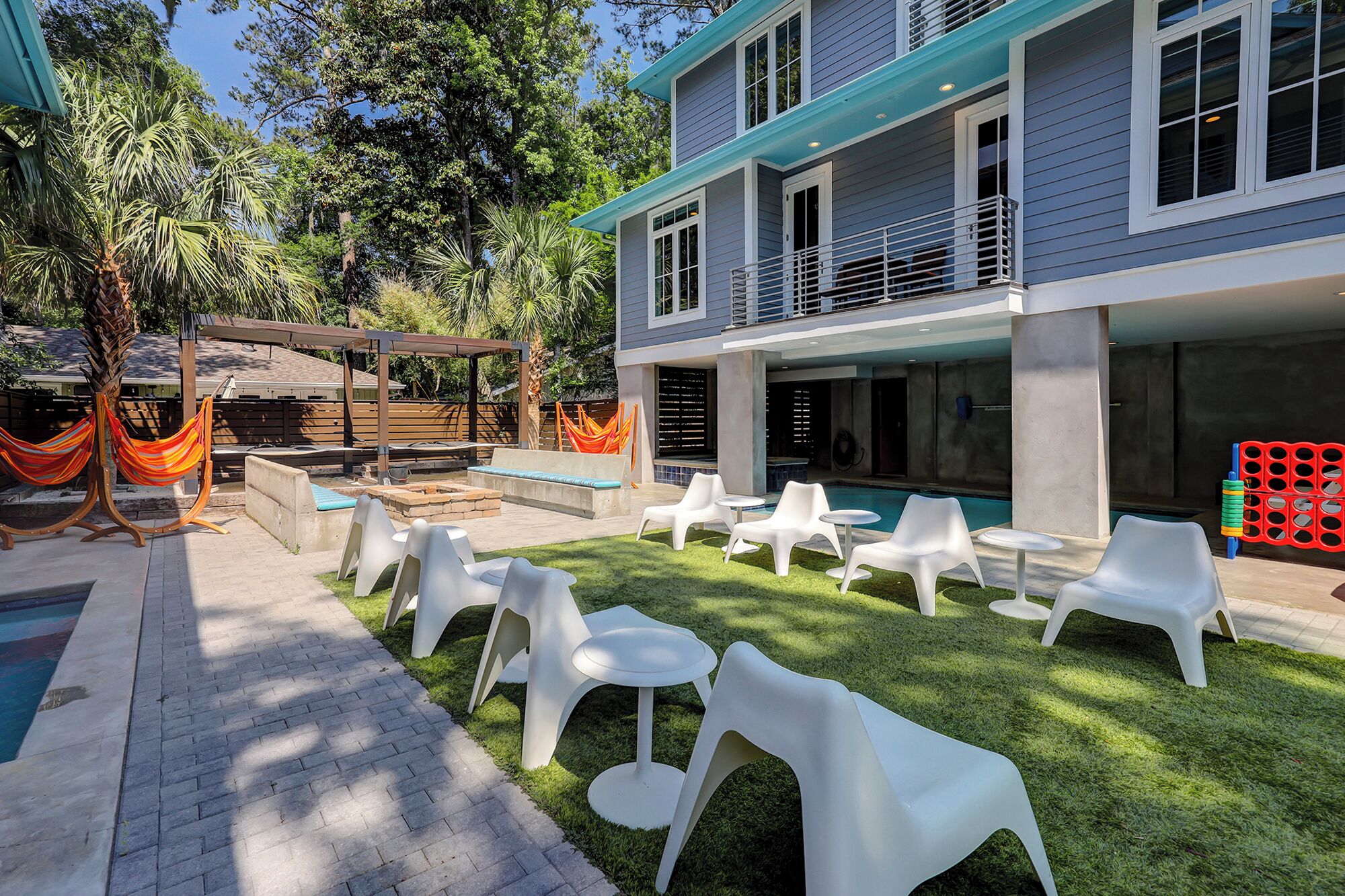 A modern outdoor patio with white plastic chairs and tables, a swimming pool, and a hammock.