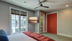 Een slaapkamer met een bed, een plafondventilator, een aan de muur bevestigde televisie en een raam met zonwering.