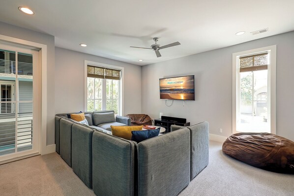 A modern living room with a sectional sofa, a bean bag, a flat-screen TV, and a ceiling fan.