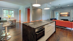 Een moderne keuken met een centraal eiland, een zithoek met oranje stoelen, en een woonruimte met een rode bank.
