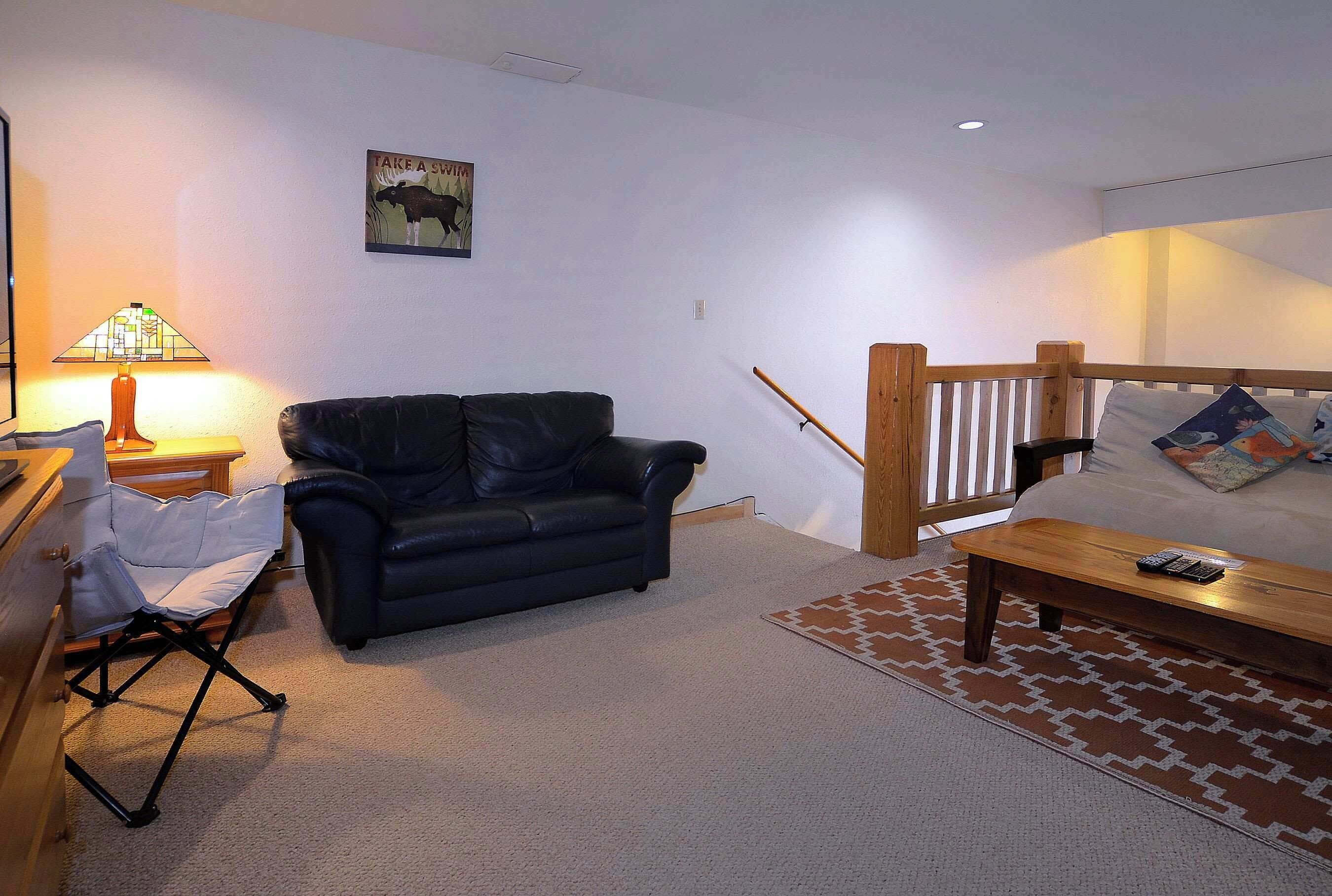 A living room with a black leather sofa, a wooden coffee table, a lamp, and a wall-mounted picture.
