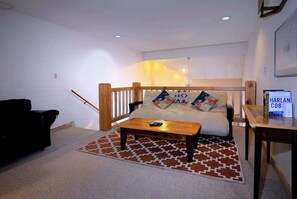 Una habitación con un sofá, una mesa de centro de madera, un tapete estampado y una mesita con un cartel.