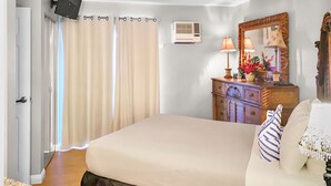 A hotel room with a bed, a ceiling fan, an air conditioning unit, a wooden dresser, a mirror, and a door with curtains. - Popular location at ocean front condo resort (Kihei)