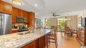 A kitchen with wooden cabinets, a granite countertop, stainless steel appliances, and a dining area with a table and chairs. - Popular location at ocean front condo resort (Kihei)