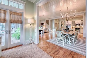 A spacious kitchen with modern appliances, a dining area with white furniture, and a large chandelier.