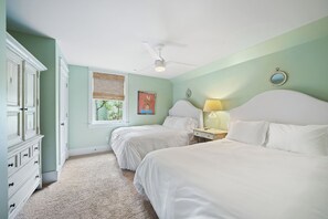 A bedroom with two beds, a ceiling fan, a window with blinds, a dresser, and a bedside table with a lamp.