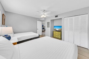 Camera d'albergo con due letti, una ventola a soffitto, una TV e vista sulla spiaggia.