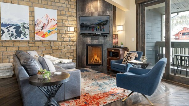 Una sala de estar acogedora con una pared de piedra, una chimenea, un televisor de pantalla plana y un amplio ventanal con vistas a una terraza.