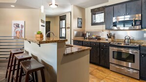 Una cocina moderna con armarios oscuros, electrodomésticos de acero inoxidable y una isla central con taburetes.