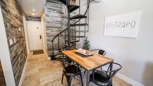 Un interior moderno con una mesa de comedor de madera, sillas negras, una escalera de caracol y una pizarra con texto.