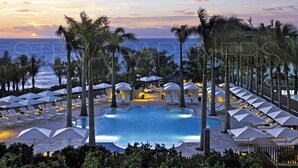 A resort pool area with lounge chairs and umbrellas, surrounded by palm trees, overlooking the ocean. - Most Luxury hotel 5 stars oceanfront w. balconies - Valet & Amenities included (Bal Harbour)