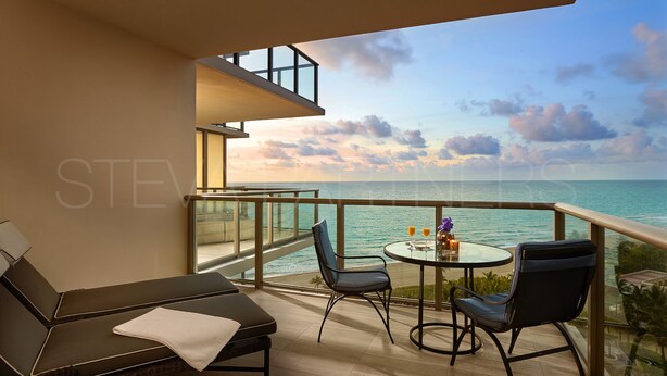 A balcony with a view of the sea, a lounge chair, two chairs, and a small table with drinks. - Most Luxury hotel 5 stars oceanfront w. balconies - Valet & Amenities included (Bal Harbour)