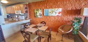 A kitchen with wooden cabinets, a microwave, and a coffee maker. There is a dining area with a glass table and chairs.
