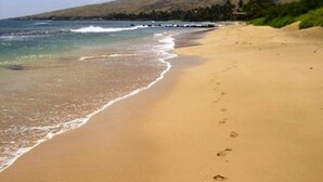 Uma praia com águas cristalinas, areal arenoso e pegadas.