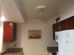 Eine Küche mit Holzschränken, einem Kühlschrank, einer Deckenleuchte und einem Wandbild einer Oldtimer.'