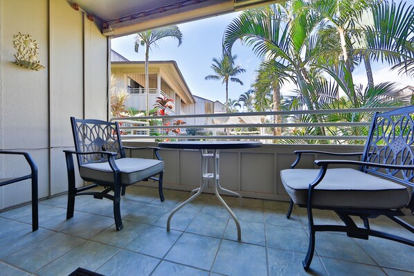 Un balcón con dos sillas y una mesa, con vista a una zona residencial con palmeras y una casa.