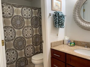 Un baño con cortina de ducha estampada, inodoro, lavamanos con artículos de aseo y espejo con marco decorado.