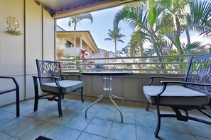 Ein Balkon mit zwei Stühlen und einem Tisch, mit Blick auf eine Wohngegend mit Palmen und einem Haus.