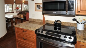 A kitchen with a stove, oven, microwave, granite countertop, wooden cabinets, and a dining area with a table and chairs. - Perfect Views and Location in Lionshead! Well Appointed Condo Steps from Lifts (Vail)