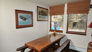 A wooden dining table with benches, framed pictures on the wall, and windows with blinds. - Perfect Views and Location in Lionshead! Well Appointed Condo Steps from Lifts (Vail)