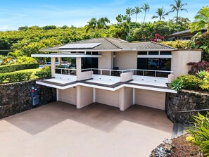 A modern house with a covered patio area, a garage, and lush greenery surrounding the property. - 🏖️Private Kona Home | Zoned A/C + 4 King Suites (Kailua Kona)