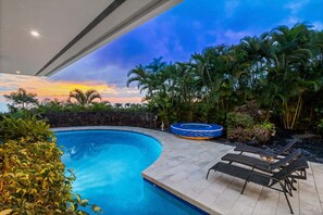Piscina con sillas de descanso y jacuzzi, rodeada de plantas tropicales y un muro de piedra.
