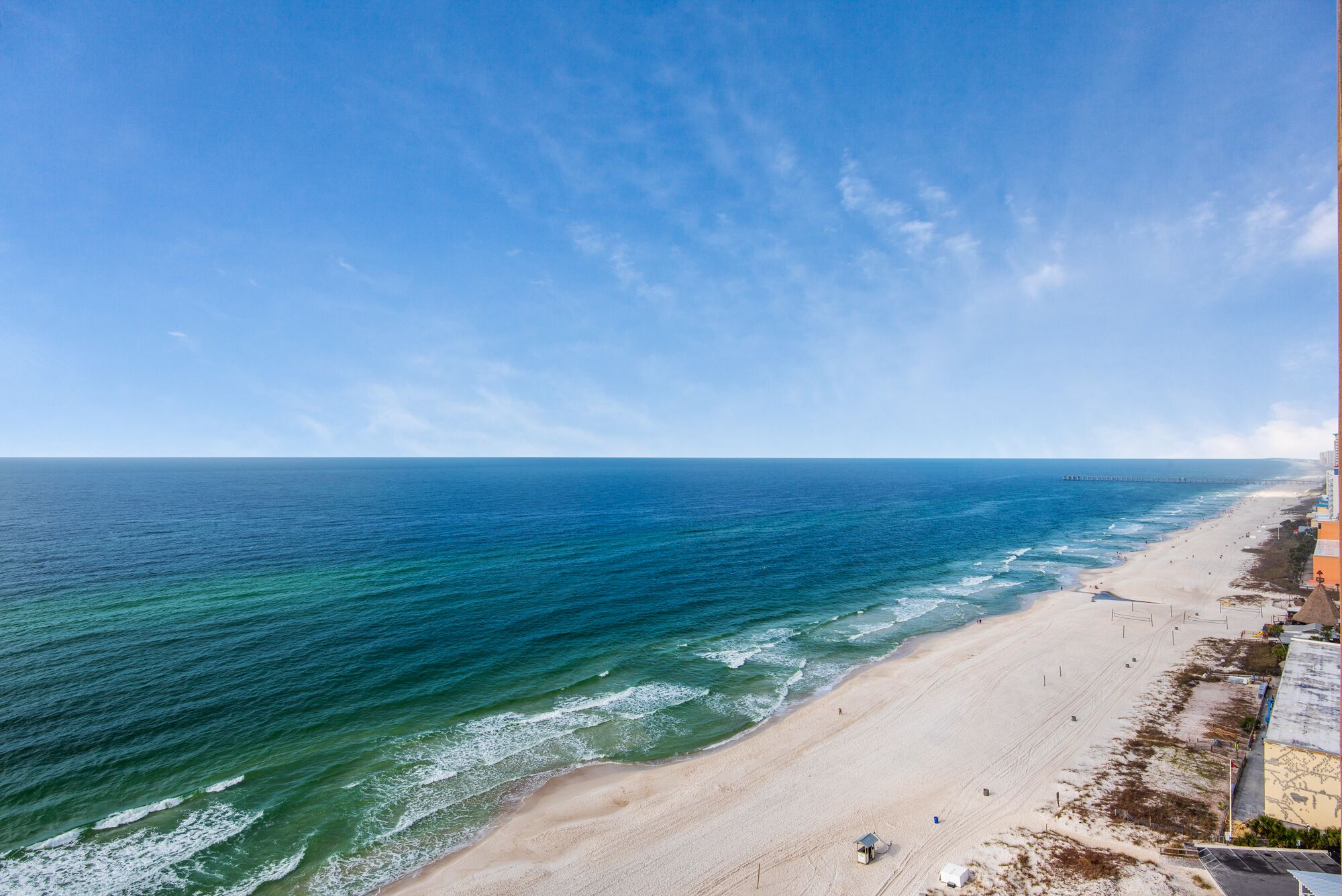 Ein Strand mit einem Steg, der ins Meer führt, sandigem Ufer und blauem Himmel.