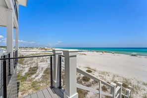 Vista a la playa desde un balcón con barandilla, arena y océano.
