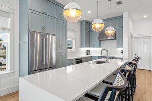 Una cocina moderna con armarios azul claro, electrodomésticos de acero inoxidable, encimera blanca e iluminación colgante.
