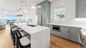 Une cuisine moderne dotée d’un îlot en marbre, de meubles gris, d’appareils électroménagers en acier inoxydable et de luminaires suspendus.