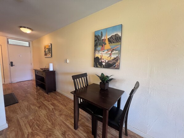 A dining area with a wooden table and chairs, a potted plant, and a painting on the wall.