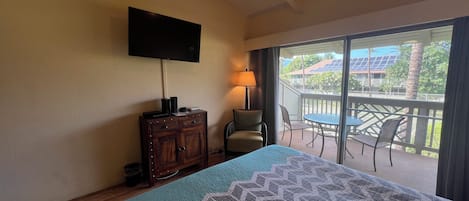 A hotel room with a bed, a TV mounted on the wall, a wooden cabinet, a chair, and a balcony with a table and chairs.