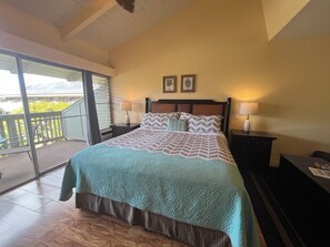 A hotel room with a bed, two bedside tables with lamps, a balcony with a view of greenery, and two framed pictures on the wall.
