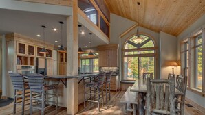 A rustic kitchen with wooden cabinets, a central island with bar stools, and a dining table with chairs. - The Lodge at Swiss Lane - TLUXP (Truckee)