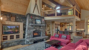 A spacious living area with a stone fireplace, a large flat-screen TV, and a cozy pink sectional sofa. - The Lodge at Swiss Lane - TLUXP (Truckee)