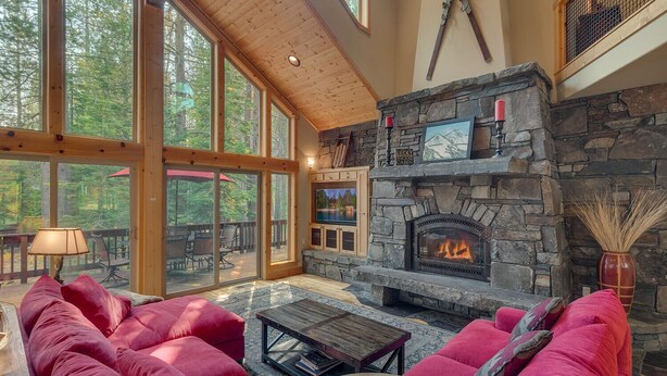 A cozy living room with a stone fireplace, large windows, and a red sofa. - The Lodge at Swiss Lane - TLUXP (Truckee)