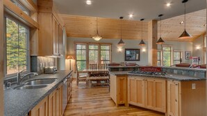 A spacious kitchen with wooden cabinets, granite countertops, and a central island. There are multiple windows providing natural light and views of the outdoors. - The Lodge at Swiss Lane - TLUXP (Truckee)