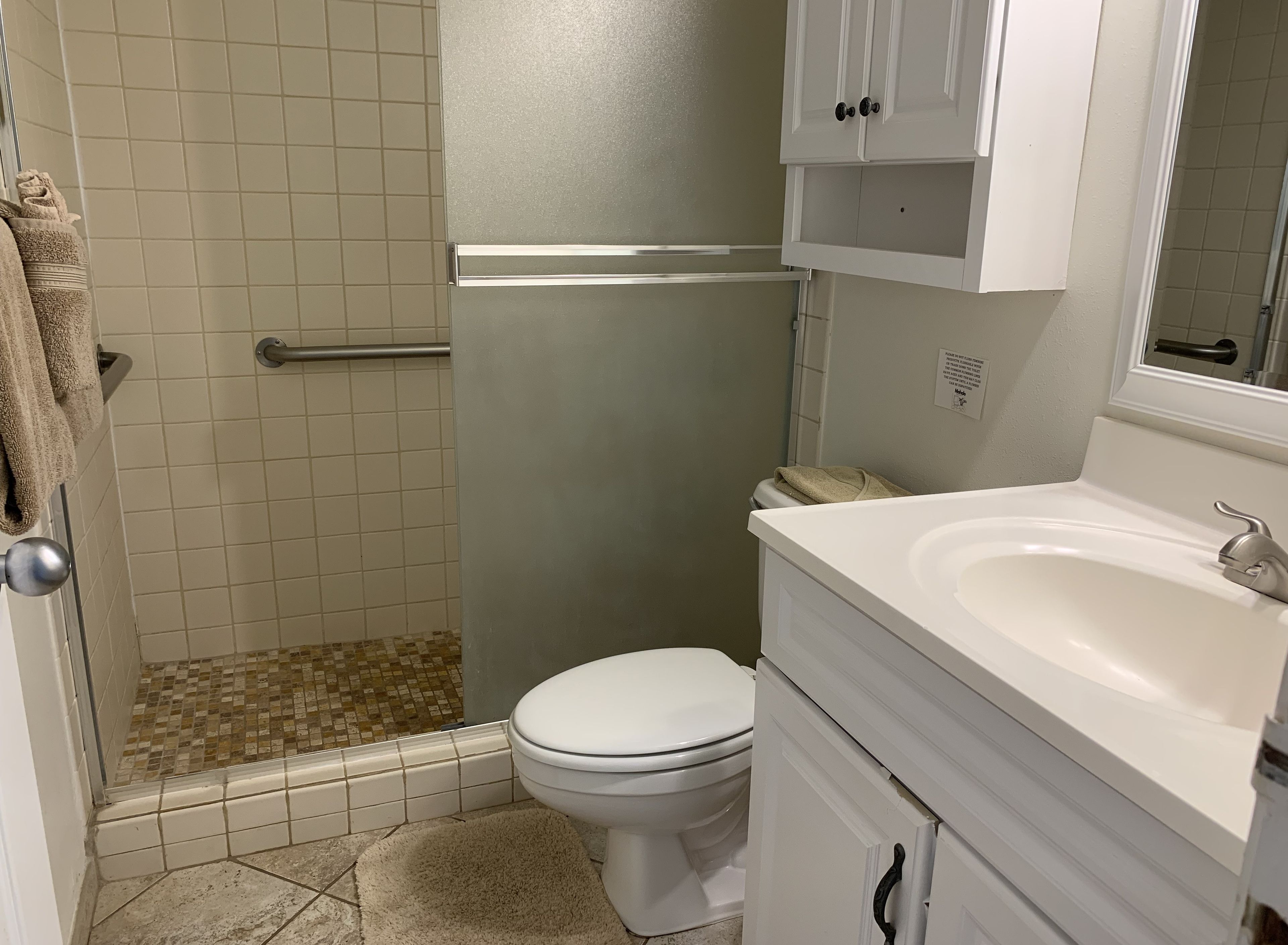 A bathroom with a shower, toilet, sink, and cabinet.