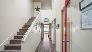 A hallway with a wooden staircase, a star decoration, and a sign indicating a beach view. - 3441O Mollies by the Sea (Oxnard)