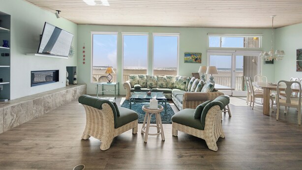 A spacious living room with wicker furniture, a large window, and a view of the beach. - 3441O Mollies by the Sea (Oxnard)