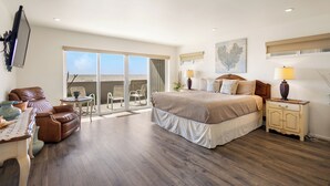 A bedroom with a large bed, a nightstand, a chair, a table, and a view of the outdoors. - 3441O Mollies by the Sea (Oxnard)