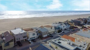 A coastal residential area with modern houses, a beach in the background, and a clear sky.