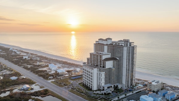 A high-rise hotel with multiple floors, a central courtyard, and a view of the ocean at sunset.