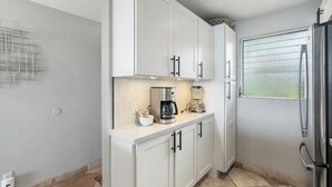 Eine moderne Küche mit weißen Schränken, einer Kaffeemaschine, einem Mixer und einem Kühlschrank.