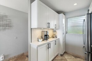 Eine moderne Küche mit weißen Schränken, einer Kaffeemaschine, einem Mixer und einem Kühlschrank.