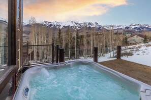 Un bain à remous avec une terrasse en bois et une vue sur des montagnes enneigées.
